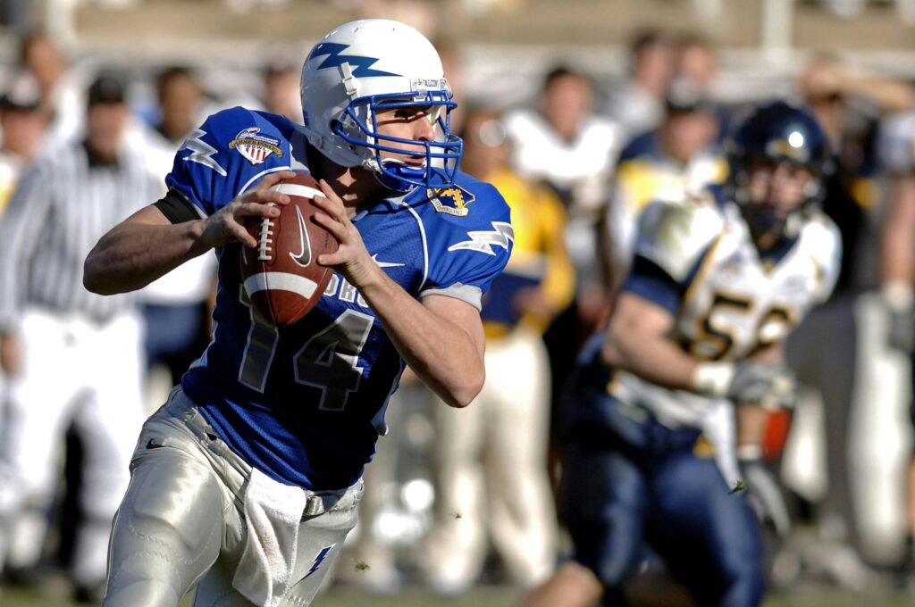 Player in blue jersey focuses on passing during a competitive football game.
